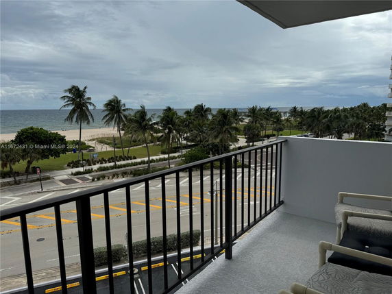 View from a balcony showing a beachfront area with palm trees and the ocean.