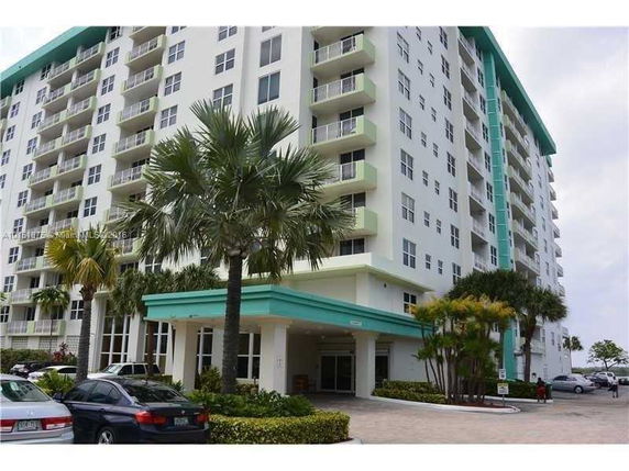 Front view of a multi-story apartment building with balconies and a palm tree outside the entrance.