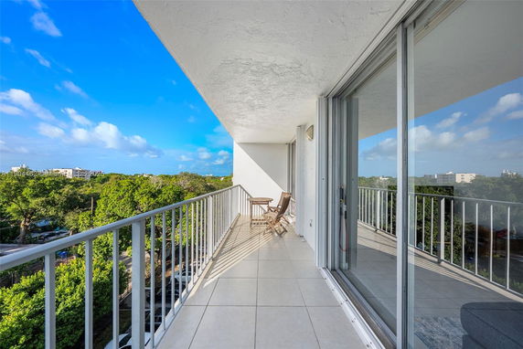 Wide balcony view from a building overlooking surrounding greenery and distant buildings.