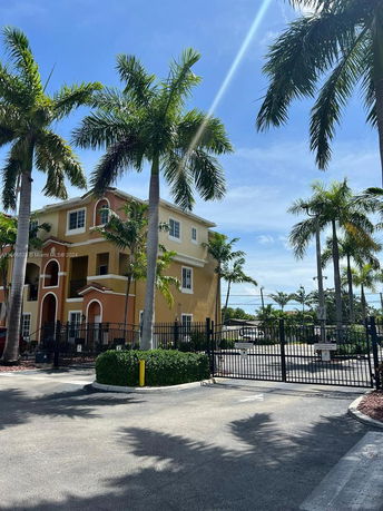 Front view of a multi-story building with gated entrance and palm trees.