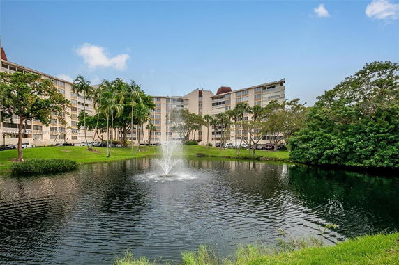 View of a multi-story apartment building with a pond and fountain in the foreground.