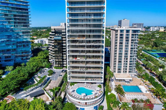 Aerial view of a modern high-rise building with a circular pool on a lower level terrace.
