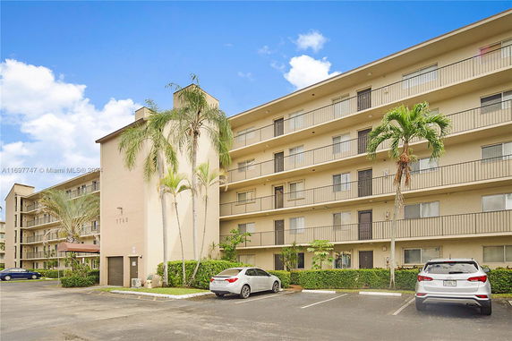 Front view of a multi-story apartment building with balconies and parking area.