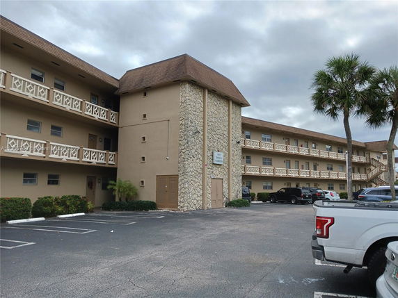 Front view of a multi-story apartment building with balconies and a parking area in front.