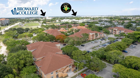 Aerial view of a residential complex with multiple buildings, parking areas, and surrounding greenery.
