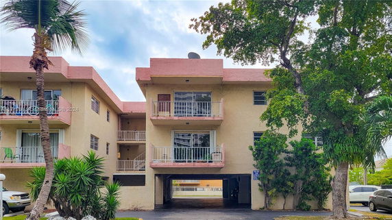 Front view of a multi-story building with balconies and parking space underneath.