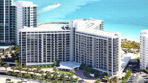 Front view of a high-rise residential building with large balconies and a white facade, situated near the ocean.