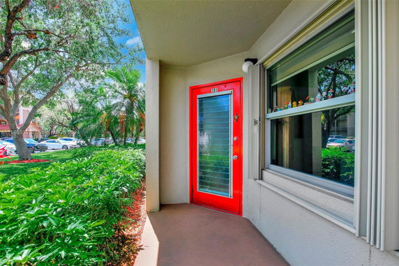 Exterior view showcasing a red door and a large window with surrounding greenery.