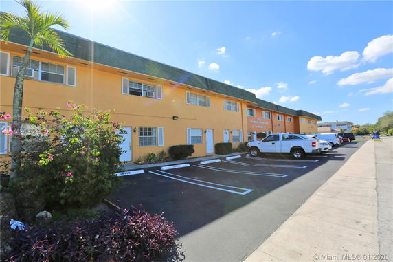 Front view of a two-story building with parking spaces and vehicles in front.