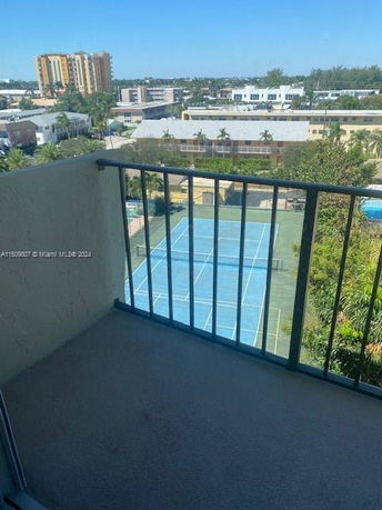 View from a building balcony overlooking a tennis court and surrounding residential buildings.