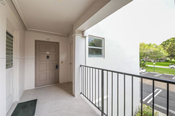 View from an apartment entrance with railing, overlooking a parking area and greenery.