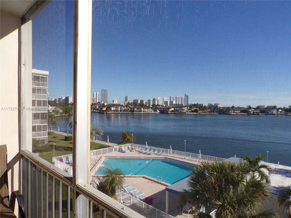 Panoramic view from a building showing a waterfront with a swimming pool and city skyline in the distance.
