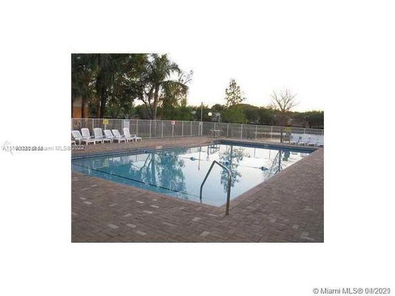 Outdoor swimming pool with surrounding fence and poolside chairs.