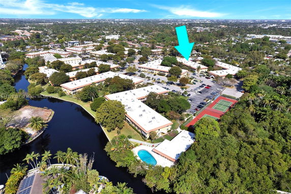 Aerial view of a residential complex with multiple buildings, parking areas, and a river.