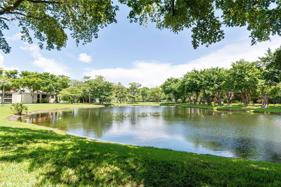 Scenic view of a pond surrounded by lush green trees and lawns.