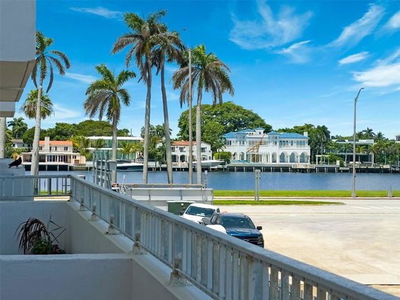 View of waterfront homes with palm trees and a body of water in the foreground.
