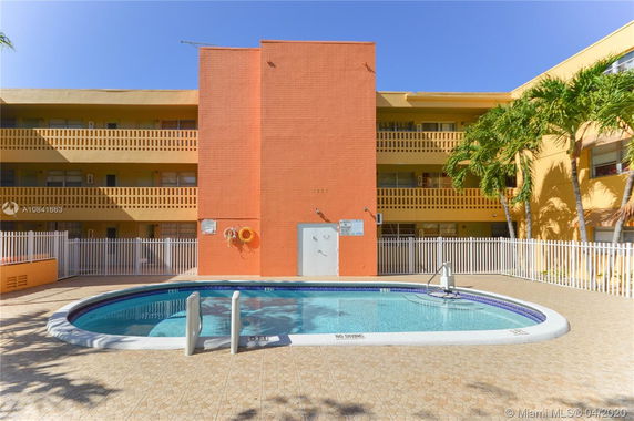 Outdoor swimming pool in front of a multi-story building with a bright orange facade.
