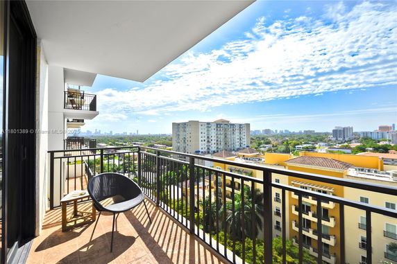 Balcony with chairs overlooking a cityscape with multiple buildings and a clear sky.
