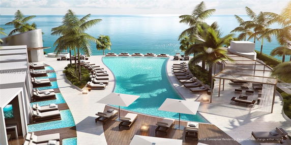 A pool area overlooking the ocean with lounge chairs and palm trees.