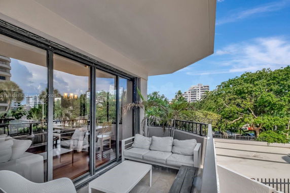 Balcony with outdoor seating overlooking a treed area and buildings.