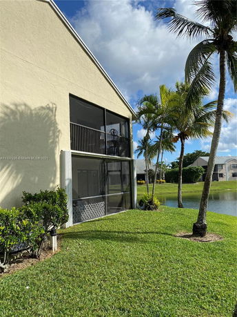 Side view of a house with screened patio and adjacent palm trees near a pond.