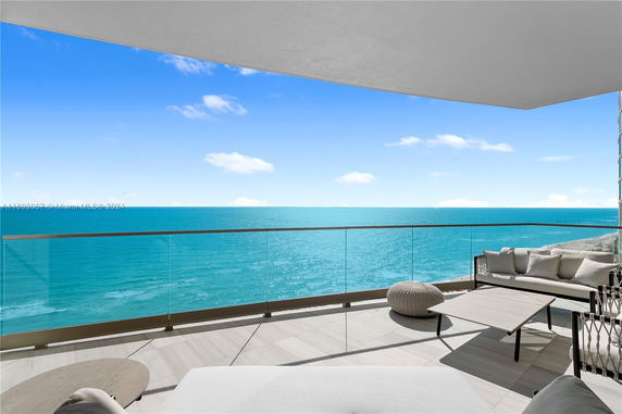 Panoramic view of the ocean from a modern balcony with glass railing and outdoor seating.