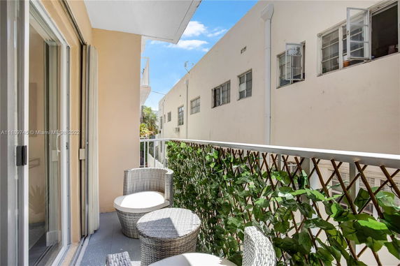 View from a balcony with wicker furniture and railing with foliage, overlooking adjacent buildings.