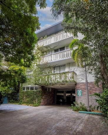 Front view of a multi-story building with balconies and ivy-covered walls.