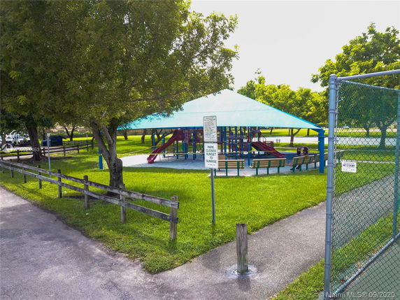 Outdoor playground with a slide and benches under a shaded structure.