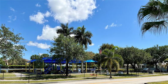 Playground with equipment under blue awnings surrounded by trees.