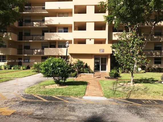 Front view of a multi-story residential building with balconies and a brick walkway leading to the entrance.