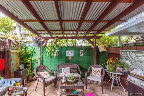 Covered outdoor seating area with wicker furniture and greenery.