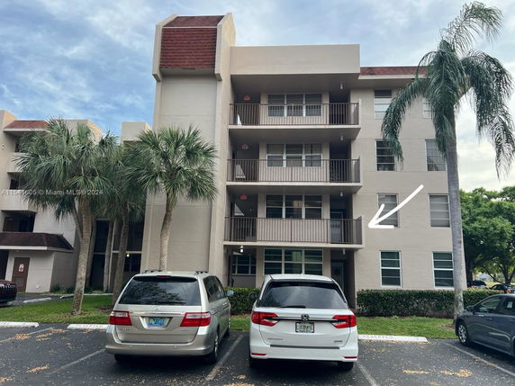 Front view of a multi-story residential building with balconies and parked cars in front.