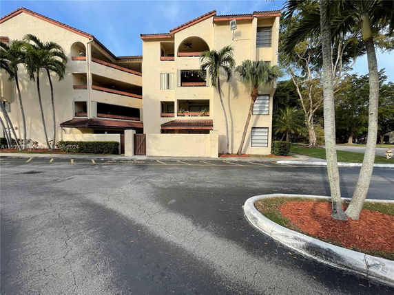 Front view of a multi-story residential building with balconies and a parking area.