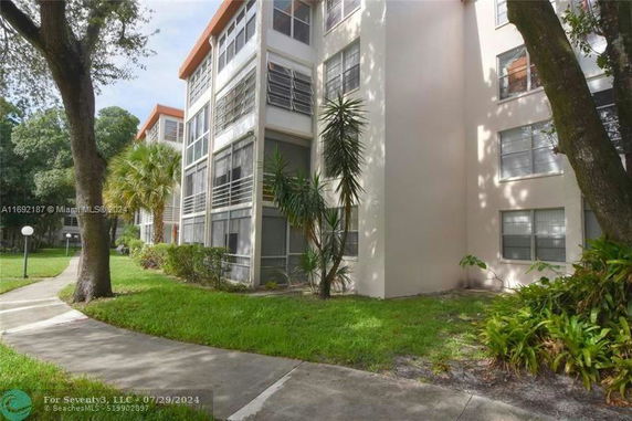 Front view of a multi-story apartment building with large windows and a landscaped area.