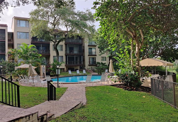 Outdoor view of a multi-story building with a swimming pool and lounge chairs in the foreground.
