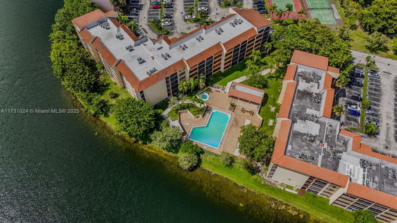 Aerial view of a residential complex with a swimming pool and parking areas by a body of water.