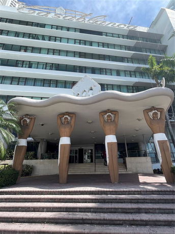 Front view of a multi-story building with a distinctive entrance featuring large human-like sculptures supporting an overhang.
