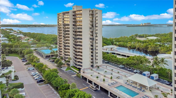 Aerial view of a multi-story residential building near a waterfront with surrounding trees and residential area.