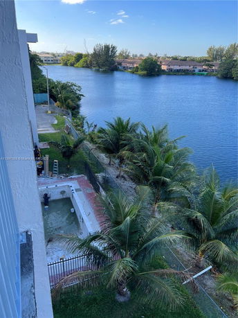 View from a building showing a pool under construction near a body of water with trees and other houses in the background.