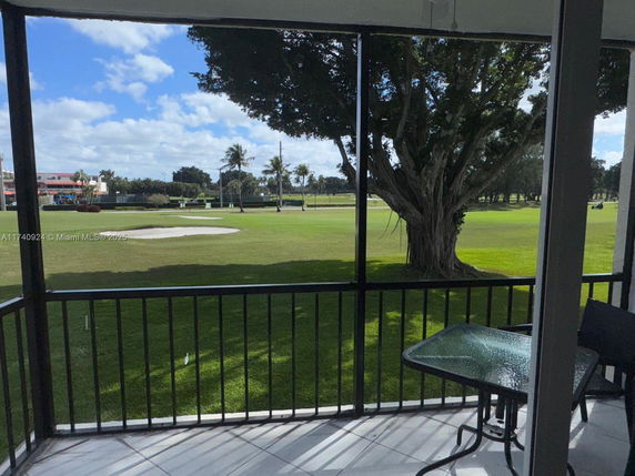 View of a golf course with a large tree and sand bunker, seen from a covered balcony.
