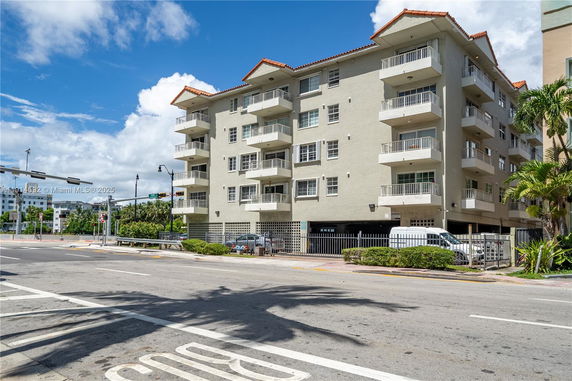 Front view of a multi-story residential building with balconies and a gated parking area.