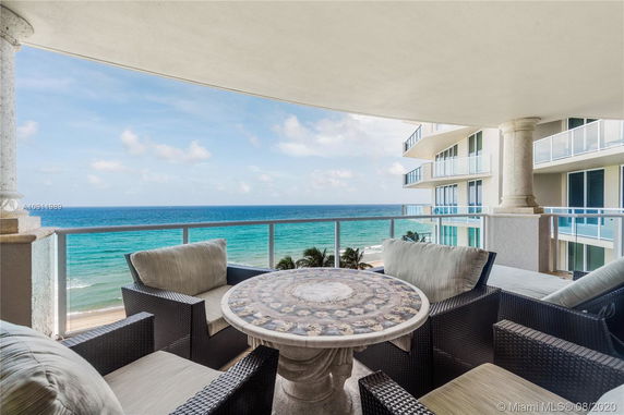 Panoramic view of the ocean from a balcony with cushioned seating and a round table.