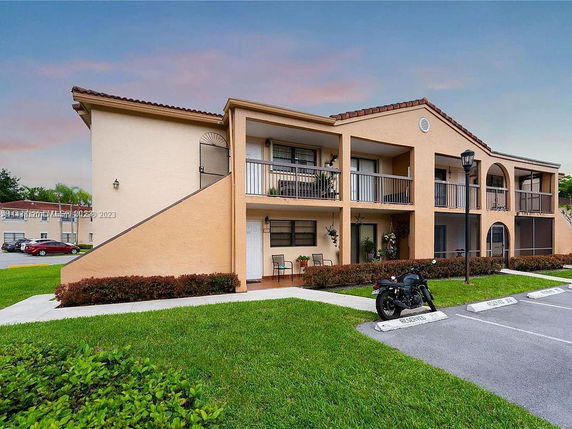 Front view of a two-story residential building with balconies and a small parking area.