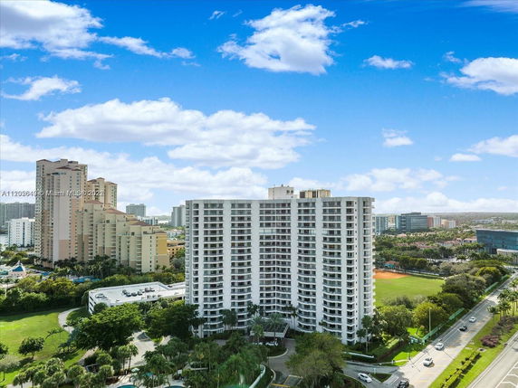 Aerial view of a tall modern apartment building with surrounding roads and greenery.