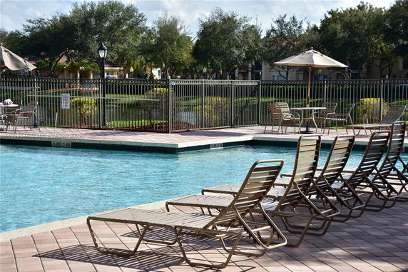 Outdoor swimming pool with lounge chairs and a fenced area.