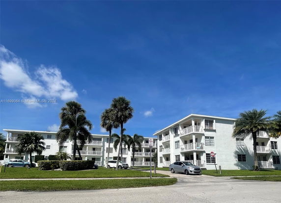 Front view of a three-story residential building with balconies and palm trees.