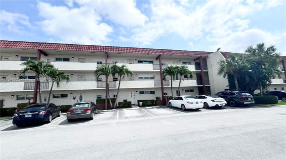 Front view of a three-story apartment building with balconies and palm trees.