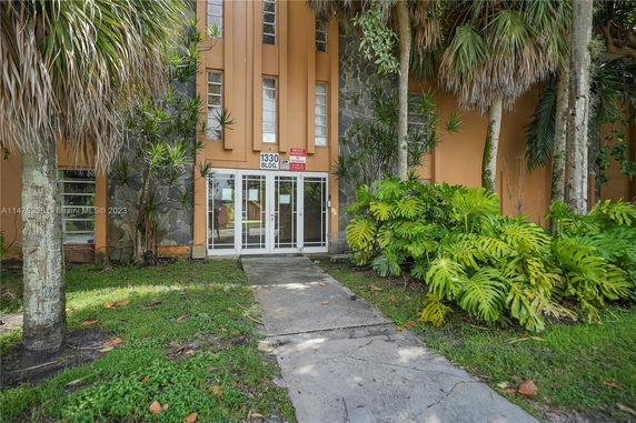 Front view of a multi-story building with glass entrance and surrounding greenery.