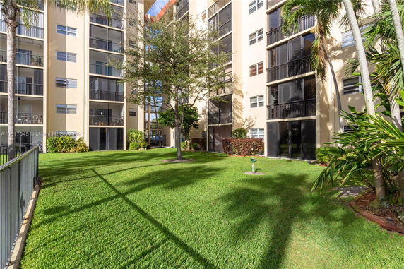 View of a multi-story apartment building with balconies and surrounding green lawn.
